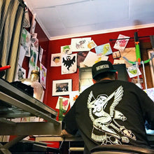 Load image into Gallery viewer, Male artist at desk wearing a tattoo style eagle and pinup t-shirt.