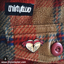 Load image into Gallery viewer, Red butt heart enamel pin on plaid flannel pocket.
