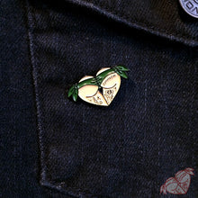 Load image into Gallery viewer, American traditional tattoo flash green scrunch butt bikini butt heart enamel pin on denim jacket.
